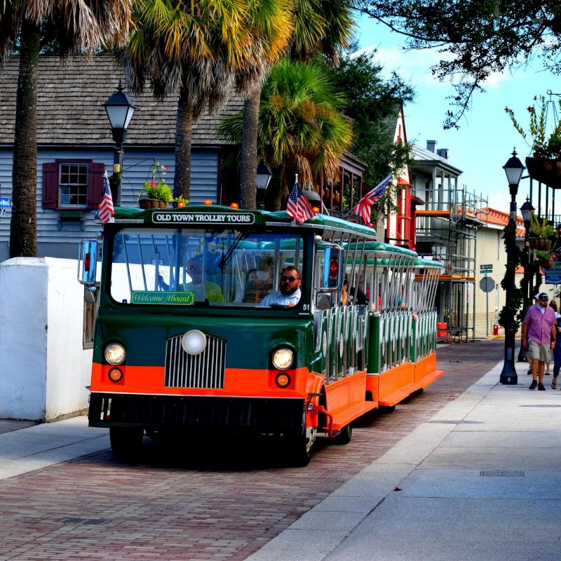 The image shows a green and orange tourist trolley driving down a street with historic buildings and palm trees in the background, ending the sentence.