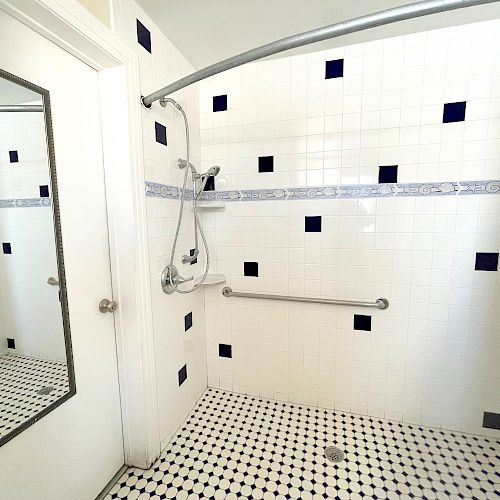 The image shows a tiled shower area with a wall-mounted showerhead, a grab bar, and a shower curtain rod. A mirror is on the adjacent door.