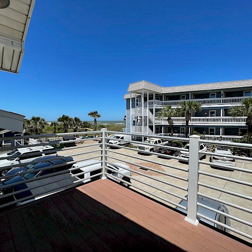 This image shows a view from a balcony overlooking a parking area with several cars and a multi-story residential building in the background.