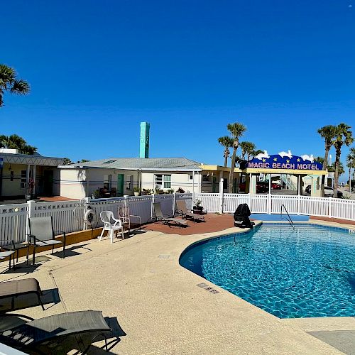 The image shows an outdoor pool area surrounded by lounge chairs and palm trees, adjacent to a building with a sign reading 