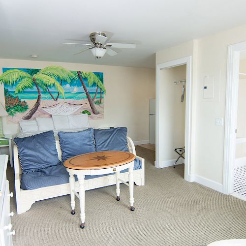 A cozy room with a beach-themed mural, a couch, a coffee table, blue curtains, and an adjoining bathroom.