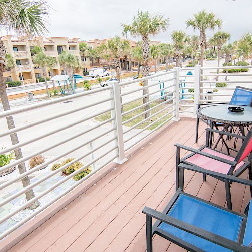 A balcony view with chairs and a table overlooking a street lined with palm trees and buildings in the background.