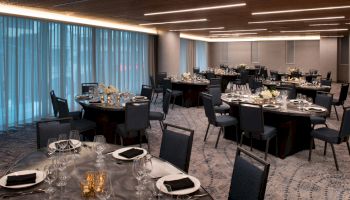 A modern banquet hall with round tables set for an event, featuring elegant table settings, glassware, candles, and floral centerpieces.