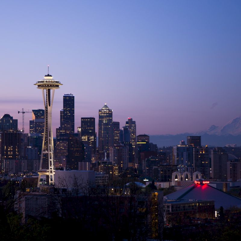 The image shows the Seattle skyline at dusk with the Space Needle prominently featured and Mount Rainier in the background.