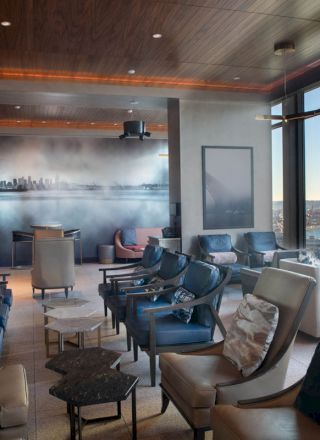 The image shows a modern lounge area with comfortable seating, large windows, and a view of a ferris wheel and water outside.