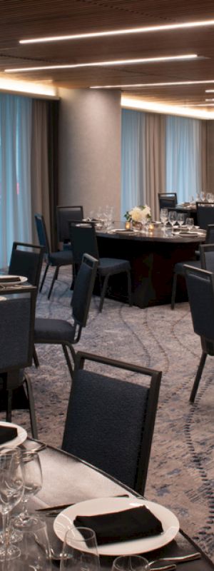 The image shows an elegant banquet hall with round tables set for an event. Each table is decorated with white flowers and black napkins.