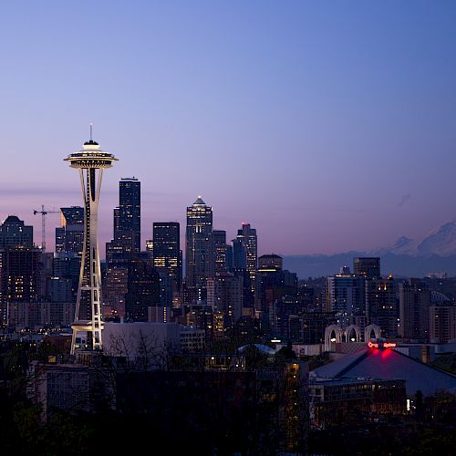 This image shows a twilight view of the Seattle skyline, featuring the iconic Space Needle and Mount Rainier in the background against a clear sky.