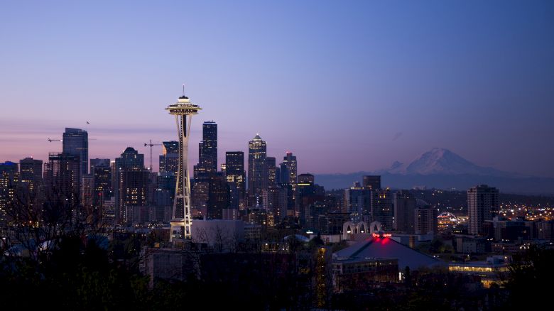 This image depicts the Seattle skyline at dusk, featuring the Space Needle and Mount Rainier in the background.