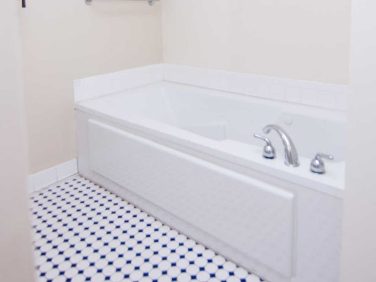 A bathroom with a white bathtub, chrome faucet, white wall tiles, and a blue and white patterned tile floor, along with a metallic towel rack.